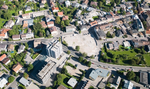 Schräg gegenüber des Dolomitenhotels soll dort, wo jetzt die kleine Grünfläche ist, die zweite Rampe aus der Kaufhausgarage führen. Auf dem Lugger-Luftbild gut zu sehen ist auch der geförderte Bauplatz südlich der Bundesstraße. Hier soll unter anderem ein Hotel Platz finden.